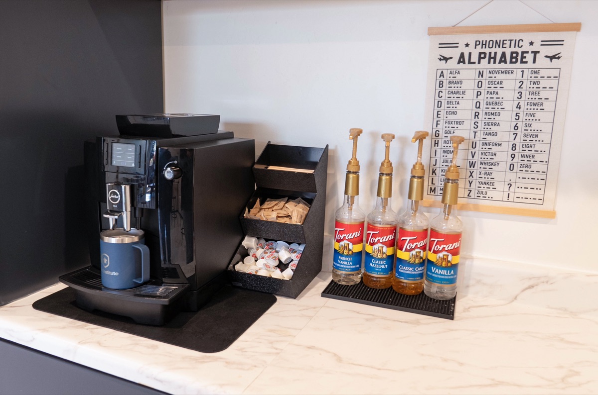 The coffee station with an espresso machine, flavor syrups and a phonetic alphabet poster