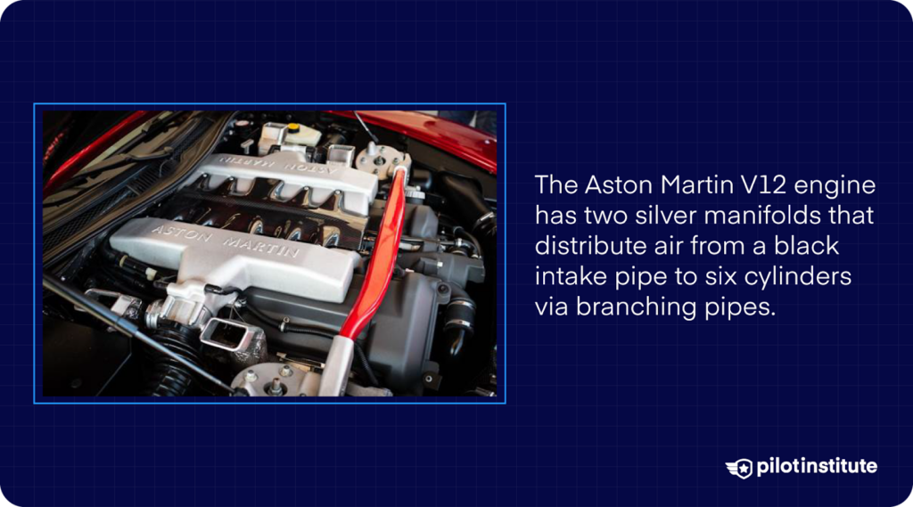 Aston Martin V12 engine with silver manifolds and a black intake pipe distributing air to six cylinders.