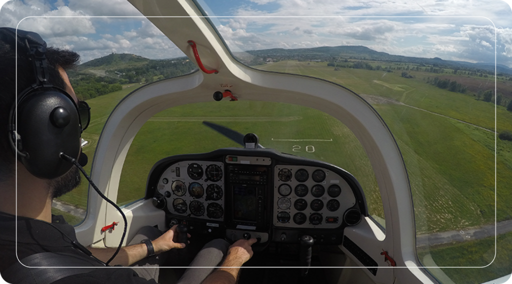 Pilot in cockpit approaching a grassy runway, showcasing flight instruments and outside view.