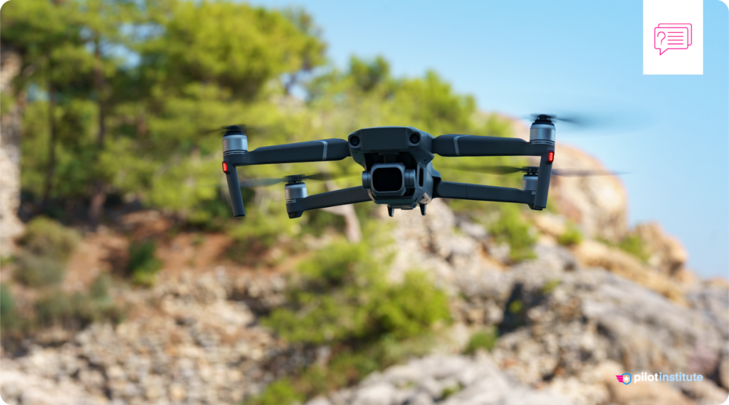 A drone hovers over a rocky, tree-covered landscape.