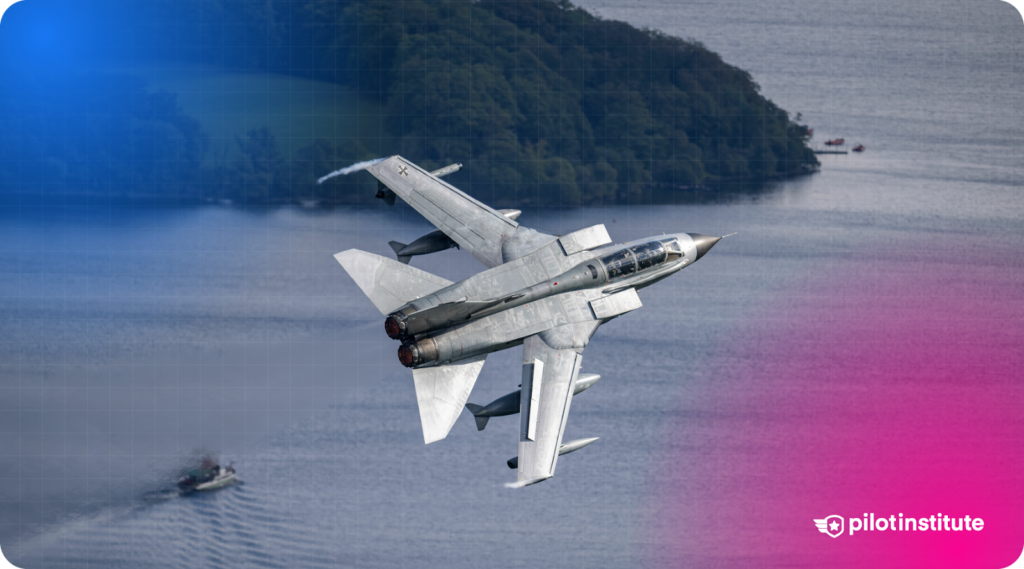 Panavia Tornado jet with variable-sweep wings banking over a body of water with a boat and forested island in the background.